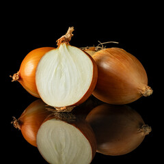 Fresh yellow onions whole and halved showing natural layers and texture on reflective black background for cooking themes