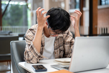 Man in plaid shirt raising curl up hands thinking or stressing in front of laptop sits at cafe table