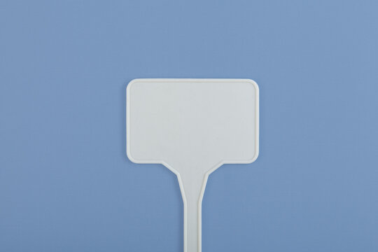 Empty plastic sign as design element. White plant stake on blue background