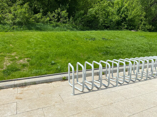 Modern bike parking stand in green park. White metal bicycle rack with curved design, installed...