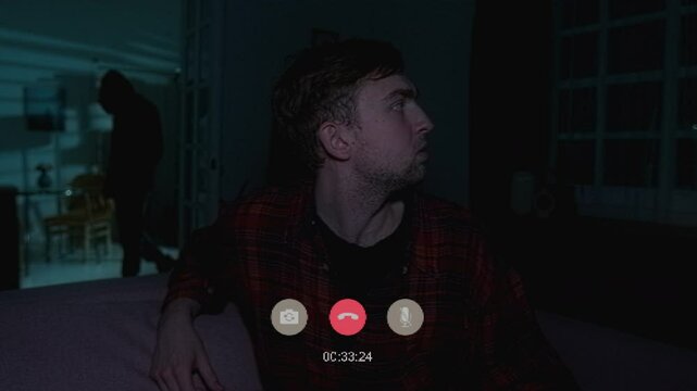 Medium shot with CGI video effects of carefree man chatting on video call with friend during lighting flashes causing blackout when spooky figure of intruder appears in hallway