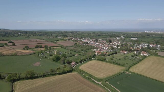 Arial view of Stogursey parish in the quantock hills Somerset. Drone slowly moving forward showing the village building and Hinkley point nuclear power station on the background.