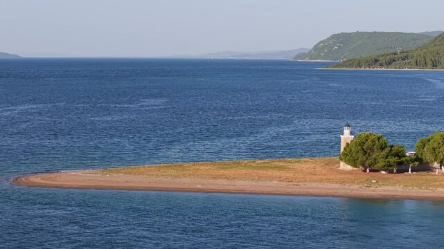 Drone moves parallel to the coast, gradually revealing the Vasilina Lighthouse in North Evia, framed by sea, rocks, and lush natural surroundings on a clear day