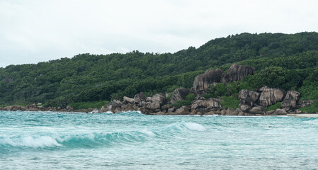Granite cliffs and dense jungle meet the turquoise waves of La Digue island in Seychelles
