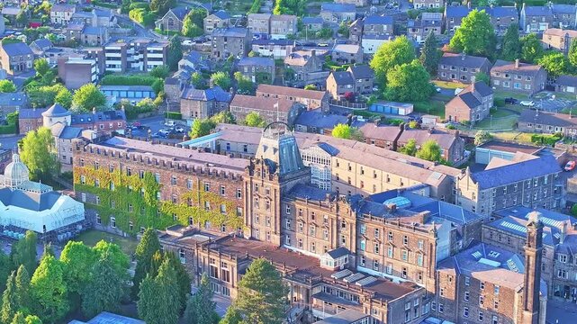 Elevated angle highlights Matlock&rsquo;s grand ivy-covered landmark at Sparrow Park, Derbyshire, with stone details, trees, rooftops, and village homes, blending heritage and community, aerial view