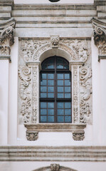 Antique baroque window with a wooden brown frame, decorated with decorative stucco on a gray wall. Jesuit Church in Lvov.