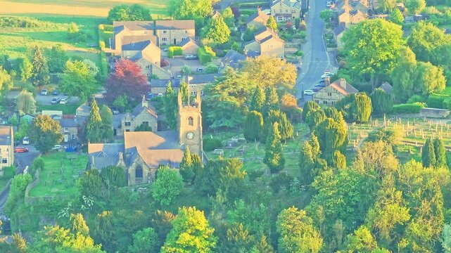 Aerial shot shows St Giles&rsquo; Church and cemetery at Matlock Sparrow Park, Derbyshire, England, framed by mature trees, cottages, winding lanes, and sunlit countryside, iconic village landmark