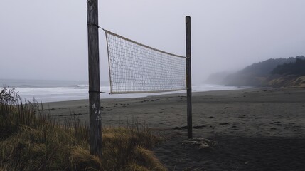 Volleyball net with visible wear set up on a foggy morning beach with mist softening the landscape and distant waves hinting at a serene but competitive scene
