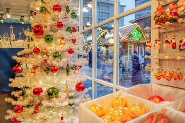 Christmas gift shop window with a wooden gingerbread house in the background and ornaments and white decorated Christmas tree on the side, Essen, Germany
