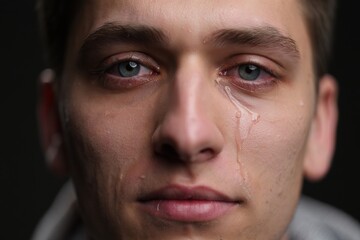 Obraz premium Close-up portrait of a young man with blue eyes and tears streaming down his face, conveying deep emotion and vulnerability in a dramatic lighting setting