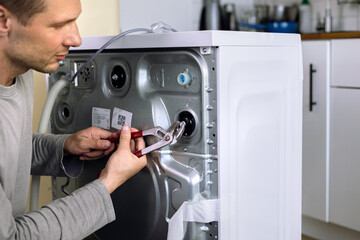 handyman repair washer at back side. washing machine repair service concept. connecting water...