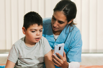 Physiotherapist showing smartphone to child with cerebral palsy during rehabilitation session