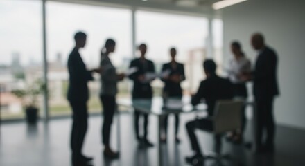 Blurred silhouettes of professionals collaborate around a table in bright, modern office setting.