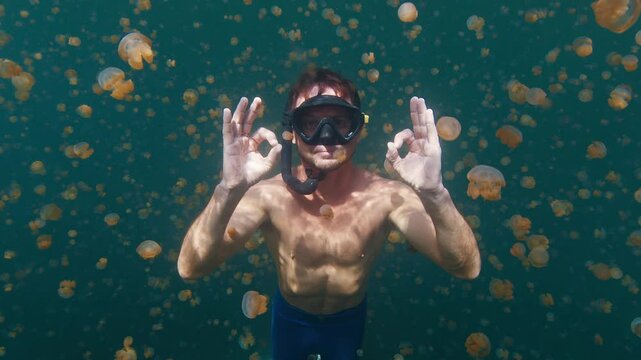 Freediver swims in the lake full of jellyfish. Male diver gently glides underwater among the millions of jellyfish