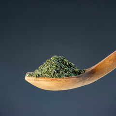 Natural wood spoon filled with dried parsley flakes, ideal for kitchen, recipe and healthy cooking concepts