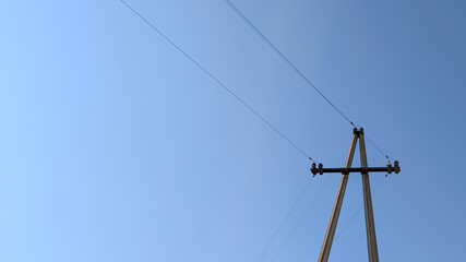 Weathered wooden power pole standing tall against azure sky, supporting electrical cables and...