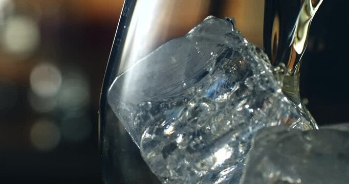 Super Slow Motion Close Up of Crystal Clear Ice Cubes in a Glass with Cold Liquid Pouring. Refreshing Beverage Preparation with Bokeh Background in Elegant Lighting 1000 fps.