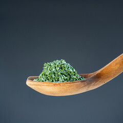 Close-up of crushed parsley or herb flakes on rustic wood utensil, ideal for culinary and food photography concepts