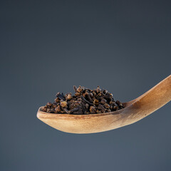 Whole dried cloves arranged on natural wooden spoon against neutral background, perfect for culinary and cooking themes