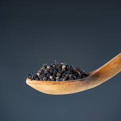 Close-up of dried black pepper corns on rustic wood utensil, perfect for gourmet food photography and spice concepts