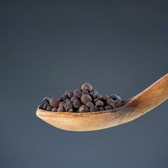 Close-up of dried pimento berries on rustic wood utensil, perfect for gourmet food photography and spice concepts