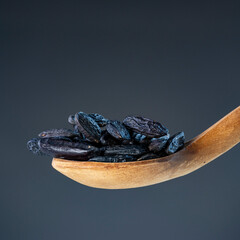 Close-up of black aromatic beans on carved wooden utensil, showcasing premium culinary ingredients and natural textures