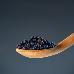 Fresh dried juniper berries in natural wood ladle, ideal for culinary herbs and aromatic cooking...