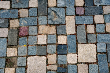 cobblestone pavement, The stones are irregularly shaped and sized, and are primarily various shades of gray and beige/tan, with a few reddish-brown stones interspersed