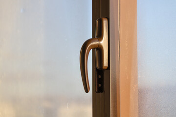 Window with a handle that is slightly open. The handle is made of metal and is slightly rusted. The window is located in a room with a view of the outside
