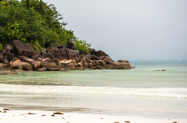 Tropical beach with white sand, calm turquoise water, lush green forest, and rocky shoreline