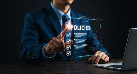 A man in a suit pointing at a digital policies checklist with a laptop on a dark wooden desk
