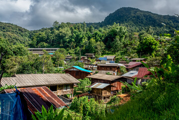 Rustic wooden village in tropical mountain landscape, nestled among dense green forest. Traditional...