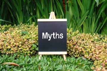 Myths writing concept on a small blackboard with a background of trees.