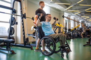 Personal trainer assists disabled sportsman in wheelchair on personal gym session showing exercise technique. Spinal injury rehabilitation, adaptive training, physical empowerment, motivation