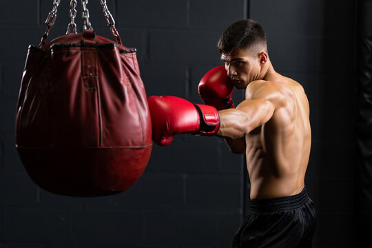 A man wearing red boxing gloves punches a red punching bag in a gym