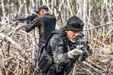 A group of military men in combat gear patrol in the middle of tropical jungle.