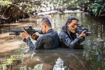 Pair of soldiers in action during river raid in the jungle waist deep in the water and mud and...