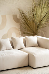A spacious living area showcases a contemporary sectional sofa adorned with cushions, complemented by a large dried palm plant in a bright and airy setting.