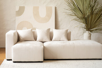 A spacious living area showcases a contemporary sectional sofa adorned with cushions, complemented by a large dried palm plant in a bright and airy setting.
