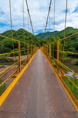 Obraz premium Yellow Iron Pedestrian Bridge Across Mountain River Against Mountain Backdrop In Vietnam