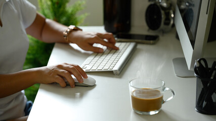 Hot coffee in a glass mug beside a computer keyboard in a cozy office environment.
