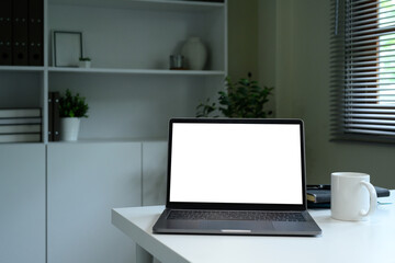 Modern workspace with blank laptop screen, coffee mug, and books on a white desk