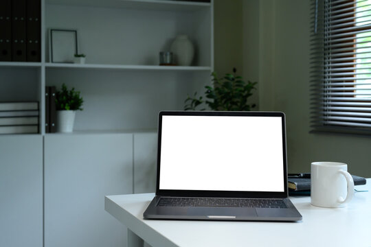 Modern workspace with blank laptop screen, coffee mug, and books on a white desk