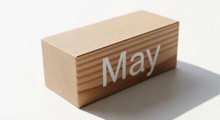 A wooden block showing the month of may sitting on a white surface with a shadow on the right side