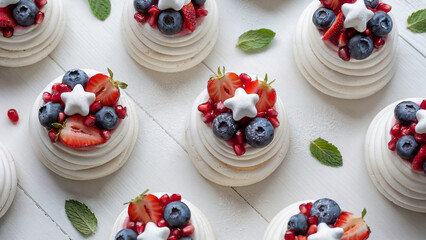 Mini pavlova desserts with whipped cream and fresh blueberries, strawberries, pomegranate seeds and small star-shaped marshmallows. Independence Day theme dessert idea.	