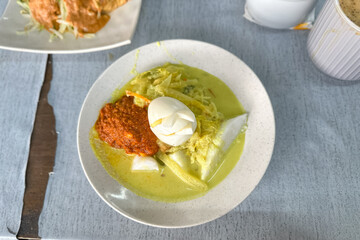 A bowl of “Lontong” or rice cake and coconut gravy with tumeric, chilli, and vegetables with some shadow and selective focus.