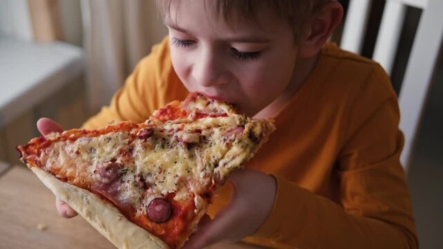Cute healthy preschool kid boy eats a piece of cheese pizza for lunch. Charming child biting off big slice of fresh made pizza at the table in a restaurant indoor. Funny little toddler. Unhealthy food