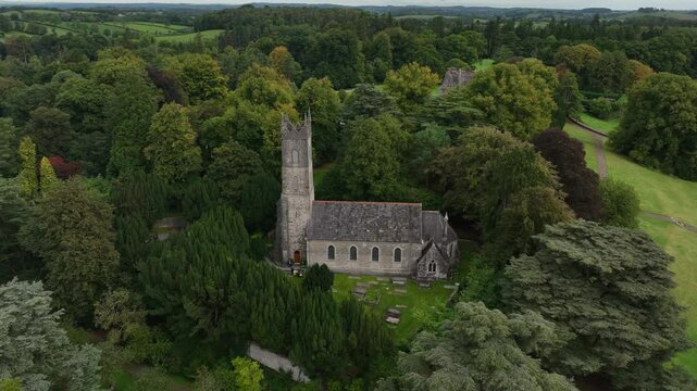 St. Salvator's Church, Glaslough, County Monaghan, Ireland, September 2022. Drone orbit clockwise and approach zoom in to tower spire of church in middle of trees.