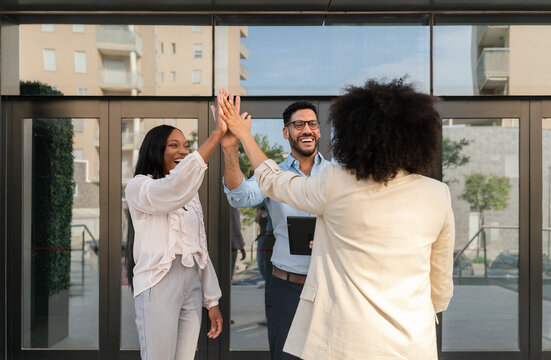 Cheerful multiethnic business team giving high five celebrating success outside office building