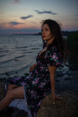 Woman in dress sitting near the lake at evening